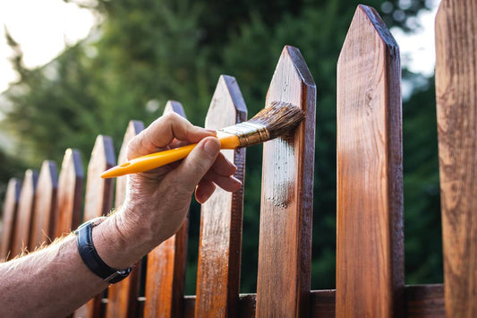 Hand applying wood stain to a garden picket fence with a paintbrush