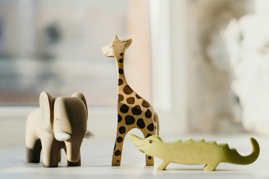 Wooden safari animal toys including an elephant, giraffe, and crocodile styled in a soft neutral nursery setting for safari themed baby room decor inspiration.