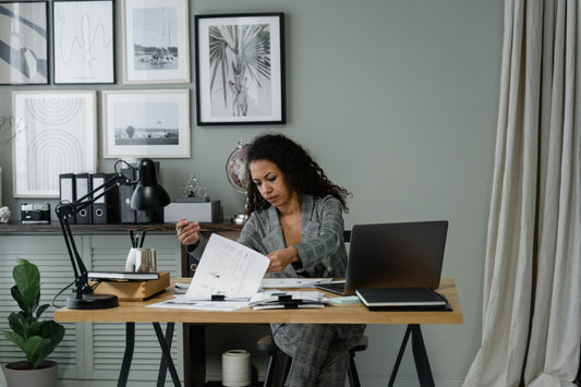 Woman working at a modern home office desk with laptop, paperwork and framed wall art on the wall